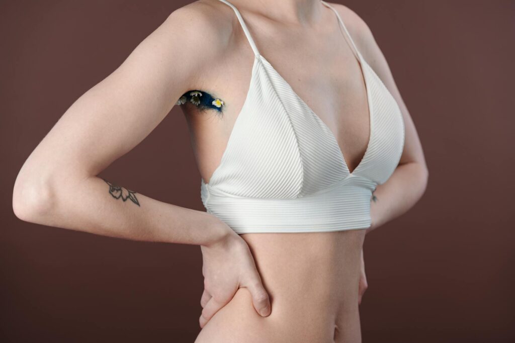 Gros plan artistique des aisselles d'une femme avec un motif floral, portant un haut court blanc.