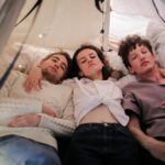 Trois adultes se détendent ensemble dans une tente intérieure douillette, profitant d'un moment de convivialité et de confort.