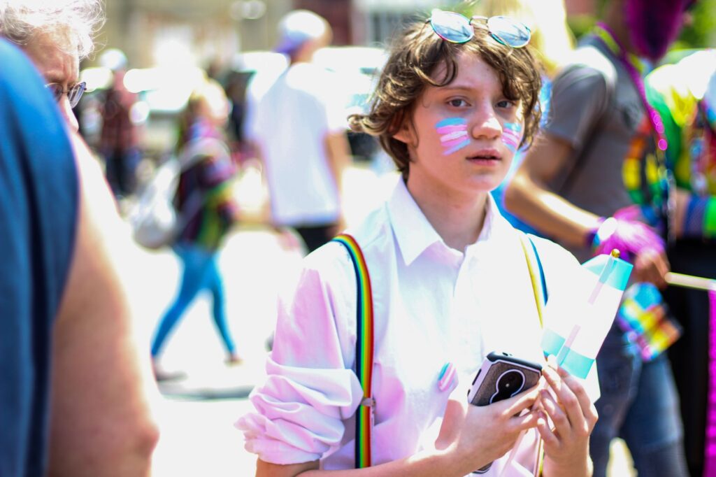 Un jeune avec du maquillage et un drapeau participe à un défilé animé de la fierté LGBTQ.