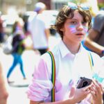 Un jeune avec du maquillage et un drapeau participe à un défilé animé de la fierté LGBTQ.